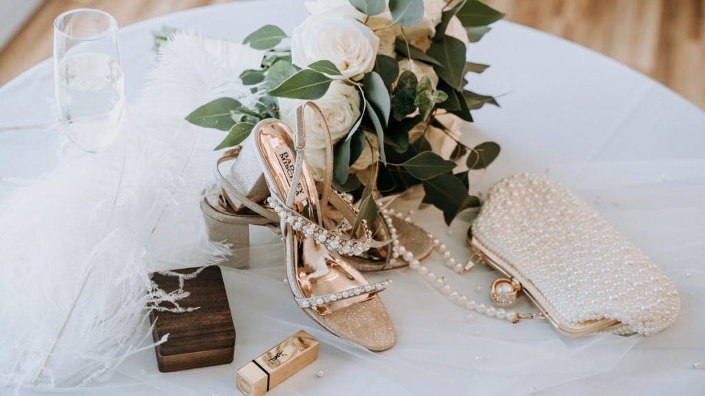 Chic bridal accessories including heels, purse, and bouquet elegantly arranged on a draped table.